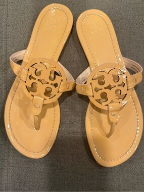 Tory Burch Patent Leather Thong Sandals  color is a pinky peach nude color.